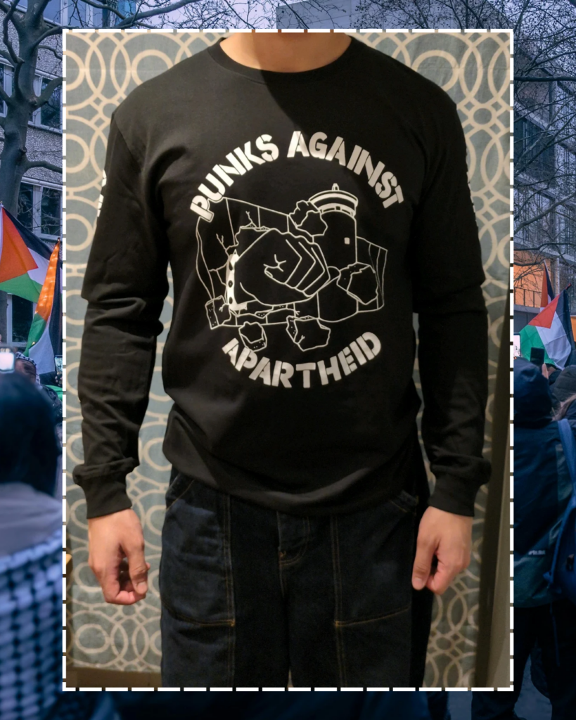 A photo of an individual facing forwards from the neck downards, showing the PAA logo (a fist with a spikey bracelet punching through the apartheid wall)..