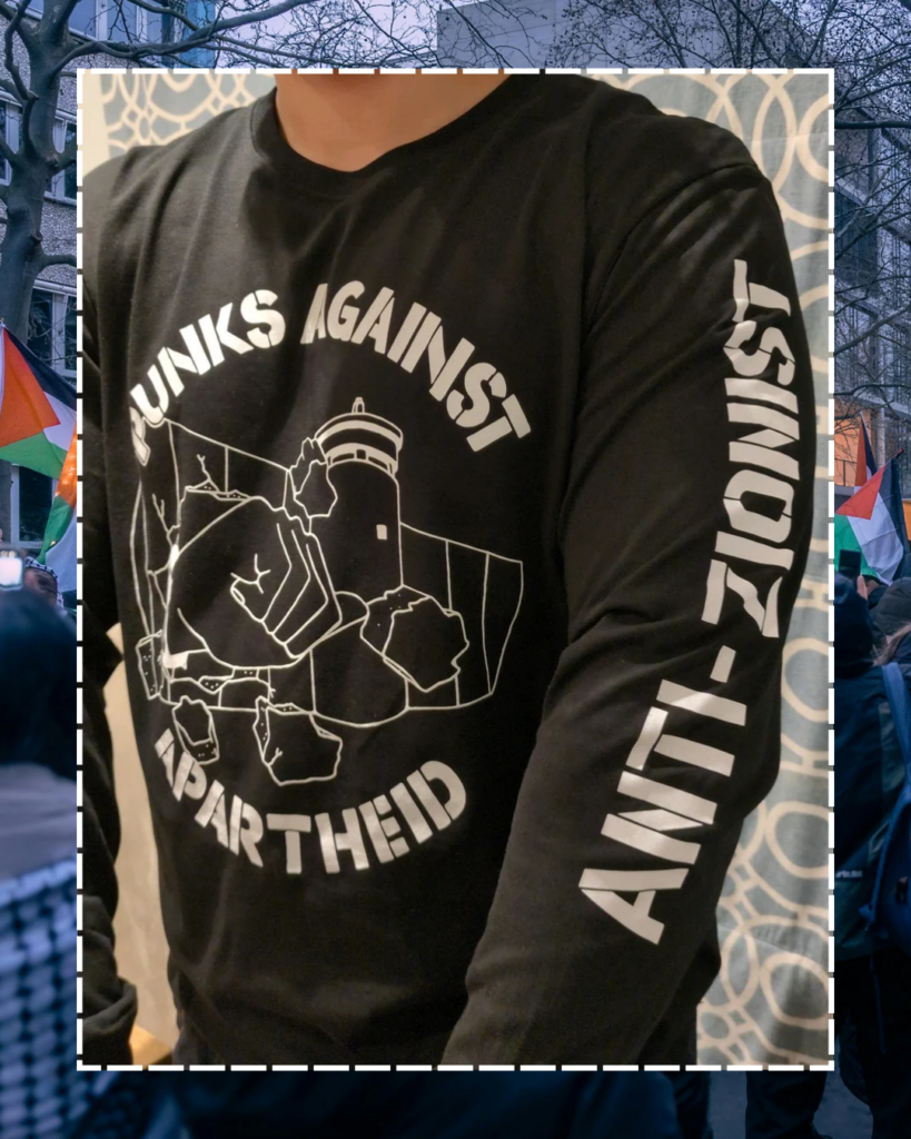 A photo of an individual facing forwards from the neck downards, showing the PAA logo (a fist with a spikey bracelet punching through the apartheid wall) & one arm which says ANTI-ZIONIST.