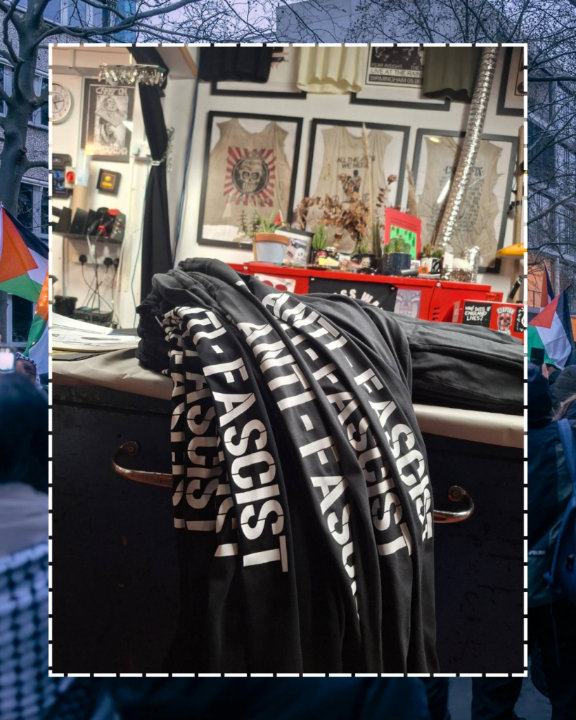 A picture of a stack of t-shirts with the sleeves showing 'ANTI-FASCIST' visible on a table in a studio with many designs and T-shirts on the wall.