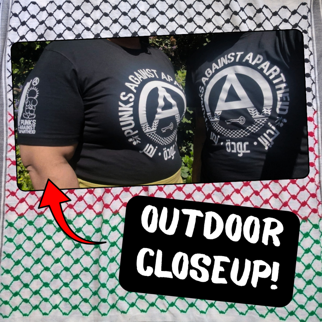 A picture of two people standing outside in front of trees showing the front and sleeve details:
A black t-shirt with a large circle (A) in the middle which fades into a keffiyyeh pattern towards the bottom. There is the silhouette of a key in the negative space at the bottom of the (A). The words PUNKS AGAINST APARTHEID ring the edge of the circle on top. On the bottom, two olive bunches on either side flank the words تجرير عودة نصر in Arabic. On the upper right sleeve (left to the viewer) there is a small map of Palestine with a keffiyyeh pattern overlaid, and a small cartoon Handhala figure, as well as a small circle (A). There is another picture of an even closer shot of the sleeve-detail and in the lower-right, 'OUTDOOR CLOSEUPS!' with arrows pointing to the images.